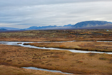 Autumn mountains and a serene lake reflect a dramatic sky with clouds, highlighting the beauty of the wild Nordic landscape, Iceland