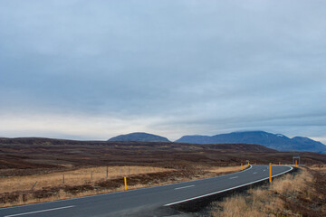 A straight desert road winds through a scenic mountain landscape under a vast summer sky, a lonely route to the horizon in Nordic landscape