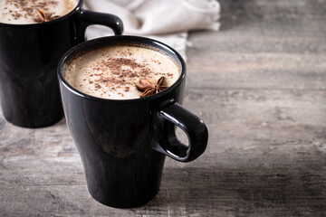 Chai Latte in Black Mug with Spices( star anise and cinnamon) on wooden table. Copy space
