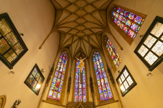 View of vibrant stained glass windows casting colorful light on a crucifix in Stadtpfarrkirche zum Heiligen Blut, Graz, Styria, Austria.