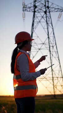 Engineer with tablet inspecting power lines at sunset for electricity infrastructure development and maintenance in rural energy sector