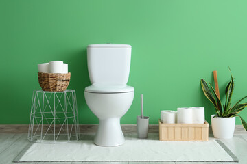 Interior of restroom with toilet bowl and organizers near green wall
