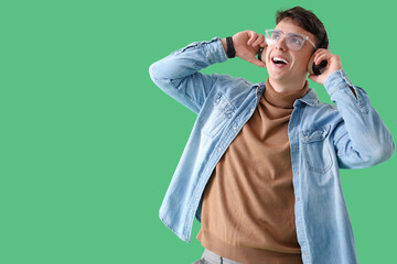 Naklejka premium Young man in headphones listening to music on green background