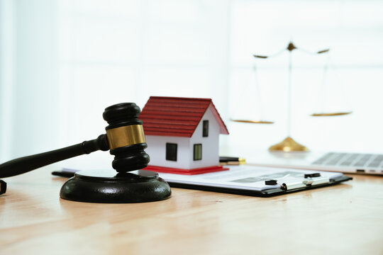A gavel, house model, and keys rest on a table beside a contract, symbolizing property sale, legal agreement, home ownership, real estate transaction, and law enforcement.A gavel, house model, and key