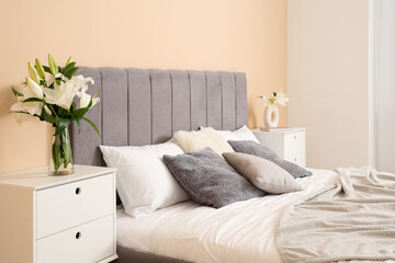 Interior of bedroom with vases of lily flowers on bedside tables near comfortable bed, closeup