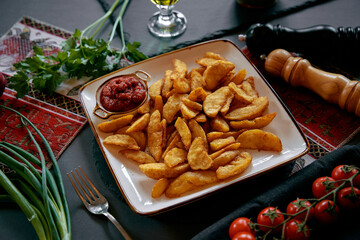 Delicious Platter of Crispy Golden Potato Wedges Served with Spicy Tomato Sauce Garnished with Fresh Herbs and Surrounded by Ingredients