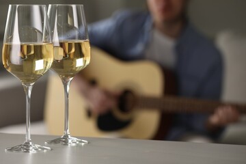 Glasses with white wine on table and man playing guitar indoors, selective focus