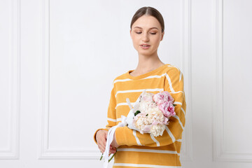 Woman with beautiful bouquet of peonies near white wall indoors, space for text
