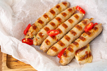 Baking paper with tasty grilled sausages, onion and chili pepper on wooden background, closeup