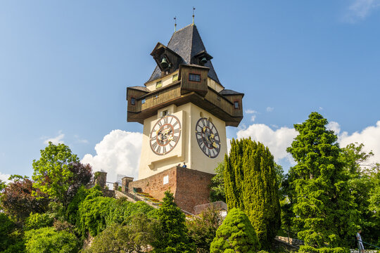 View of the iconic clock tower soaring over lush greenery, standing as a testament to history against the clear sky, Graz, Styria, Austria.