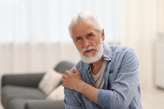 Senior man suffering from shoulder pain at home - Powered by Adobe