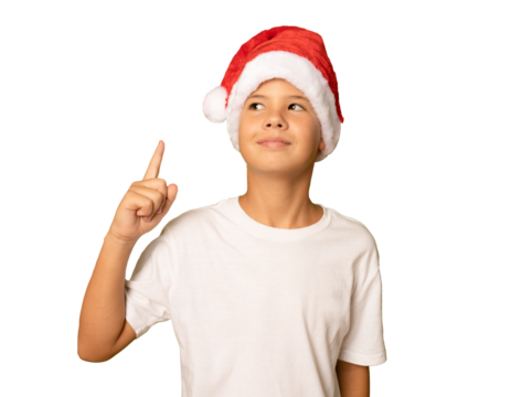 Portrait of a child boy in santa Claus hat and white t-shirt pointing and looking up over transparent background. PNG. Christmas.