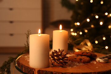 Composition with burning candles, cookies and decorations on table against Christmas tree indoors