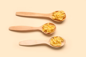 Wooden spoons with raw pasta shells on beige background
