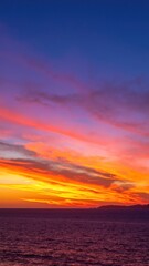 Fototapeta premium A vibrant sunset paints the sky in hues of orange, pink, and purple, reflecting beautifully on the calm ocean waves, creating a serene coastal scene.