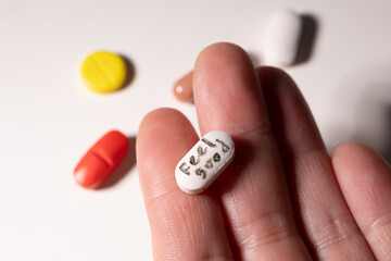 A person holds a white capsule in their hand, surrounded by colorful pills of various shapes.