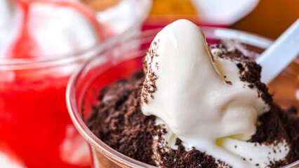 Creamy vanilla soft serve ice cream topped with chocolate cookie crumbs in a plastic cup.