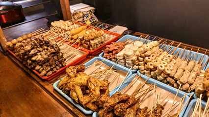 A variety of street food called angkringan, skewered and fried foods, are displayed on blue trays on wooden tables, ready to be served