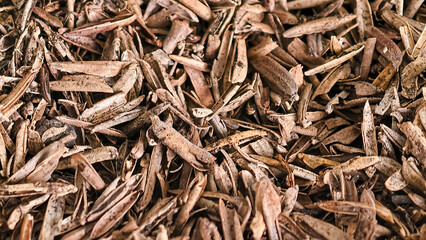 Close-up view of the texture of a pile of dry, brown and yellowish-brown mulch flakes scattered randomly.