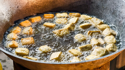 Deep-fried tofu cubes sizzle and bubble in a large wok filled with hot oil.