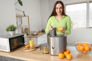 Young woman making orange juice at table in kitchen