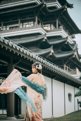 Young Asian woman in traditional attire near a large building.