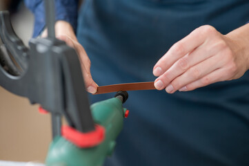 Leatherworker grinding the edge of a strip of leather for a belt in the workshop. 