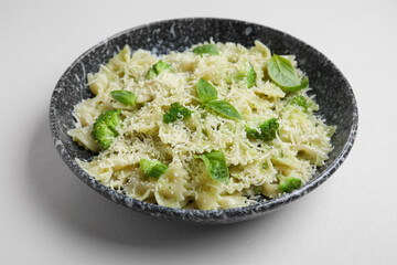 Bowl of delicious farfalle pasta with broccoli and basil leaves on grey background