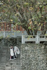 Obraz premium Young Asian female in traditional attire with parasol outdoors.