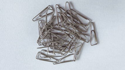 A pile of metallic paperclips scattered on a white surface.
