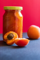 A home made apricot jam and fresh apricots nearby. Red background. Apricot jam in a jar.