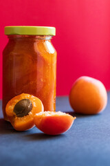 A home made apricot jam and fresh apricots nearby. Red background. Apricot jam in a jar.