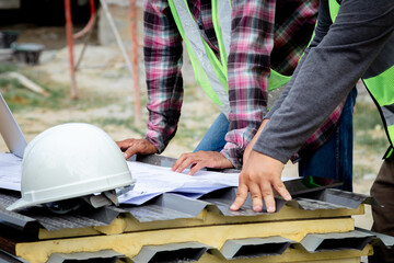Asian overweight foreman working on construction site wearing safety white helmet consult contractor male middle-aged partnership, two Asian worker inspects blueprint paperwork using laptop technology