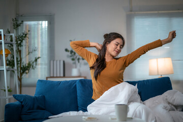 Young woman stretching on sofa after waking up in cozy living room