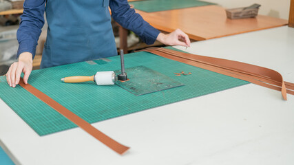 Woman tanner processes the edges of a leather belt in a workshop. 