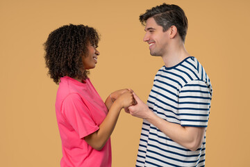 Love confession. Happy interracial couple stands on beige, holding hands