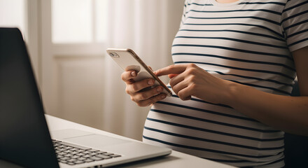 Woman Holding Smartphone Typing At Desk with Laptop and Striped Shirt in Bright Indoor Setting
