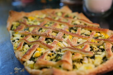 A slice of baked savory pastry with a lattice top and spinach filling sits on a colorful plate against a wooden surface