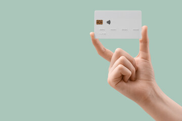 Female hand with credit card on light turquoise background, closeup