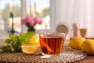 Cup of hot aromatic tea, lemons and fresh mint on table at home