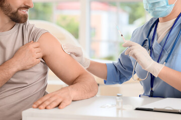 Young man receiving vaccine from doctor at table in clinic, closeup