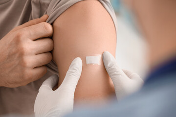Young man with doctor applying medical patch after vaccination in clinic, closeup