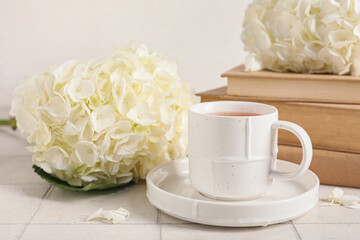 Beautiful hydrangea flowers with cup of tea and books on tile table against light wall