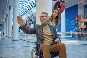 Woman gently pushes a man in a wheelchair down a long hallway
