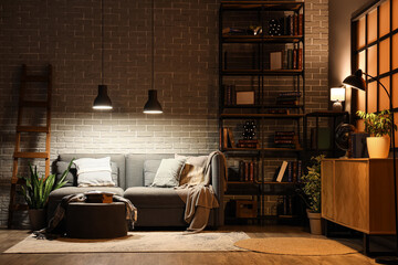 Interior of living room with bookshelf, sofa and glowing lamps at night