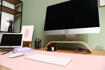 Stylish workplace with modern computer, other devices and stationery on wooden desk indoors, low angle view