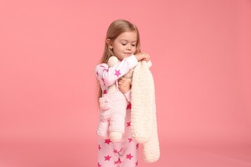 Cute little girl in pajamas with toy bunny on pink background