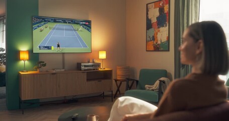 Young Woman Watching Sports Live Channel with a Female Tennis Tournament Broadcast. She is Sitting on a Couch at Home and Enjoying the Program. Zoom Out Speed Ramp Footage - Powered by Adobe
