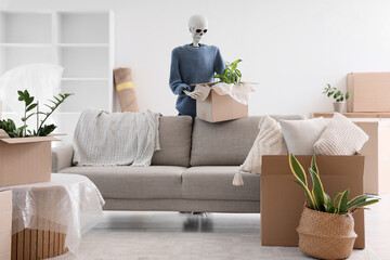 Human skeleton model with cardboard box near sofa in living room on moving day