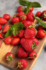 Wooden board with sweet ripe strawberries and mint leaves on grey background, closeup